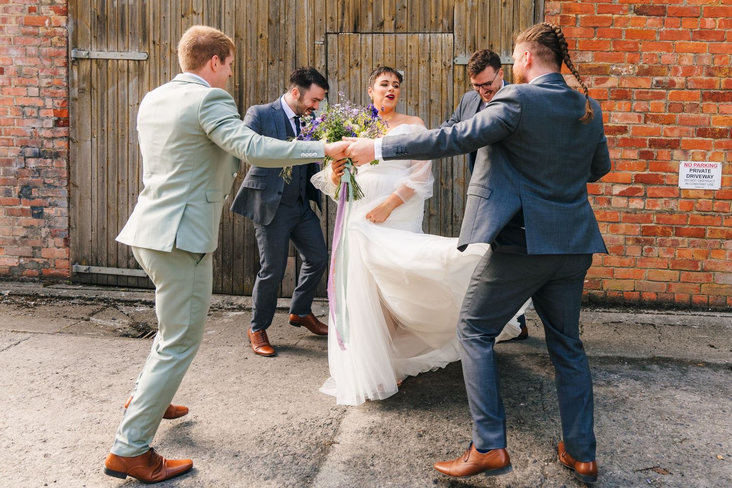 A wedding party in formal attire playfully poses together against a rustic brick wall.Millhouse slane wedding photographer dublin