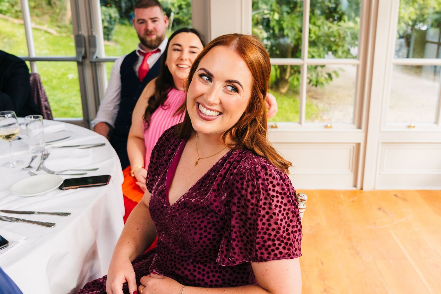 Millhouse slane wedding photographer dublinWedding guest in burgundy dress smiles warmly at reception table.
