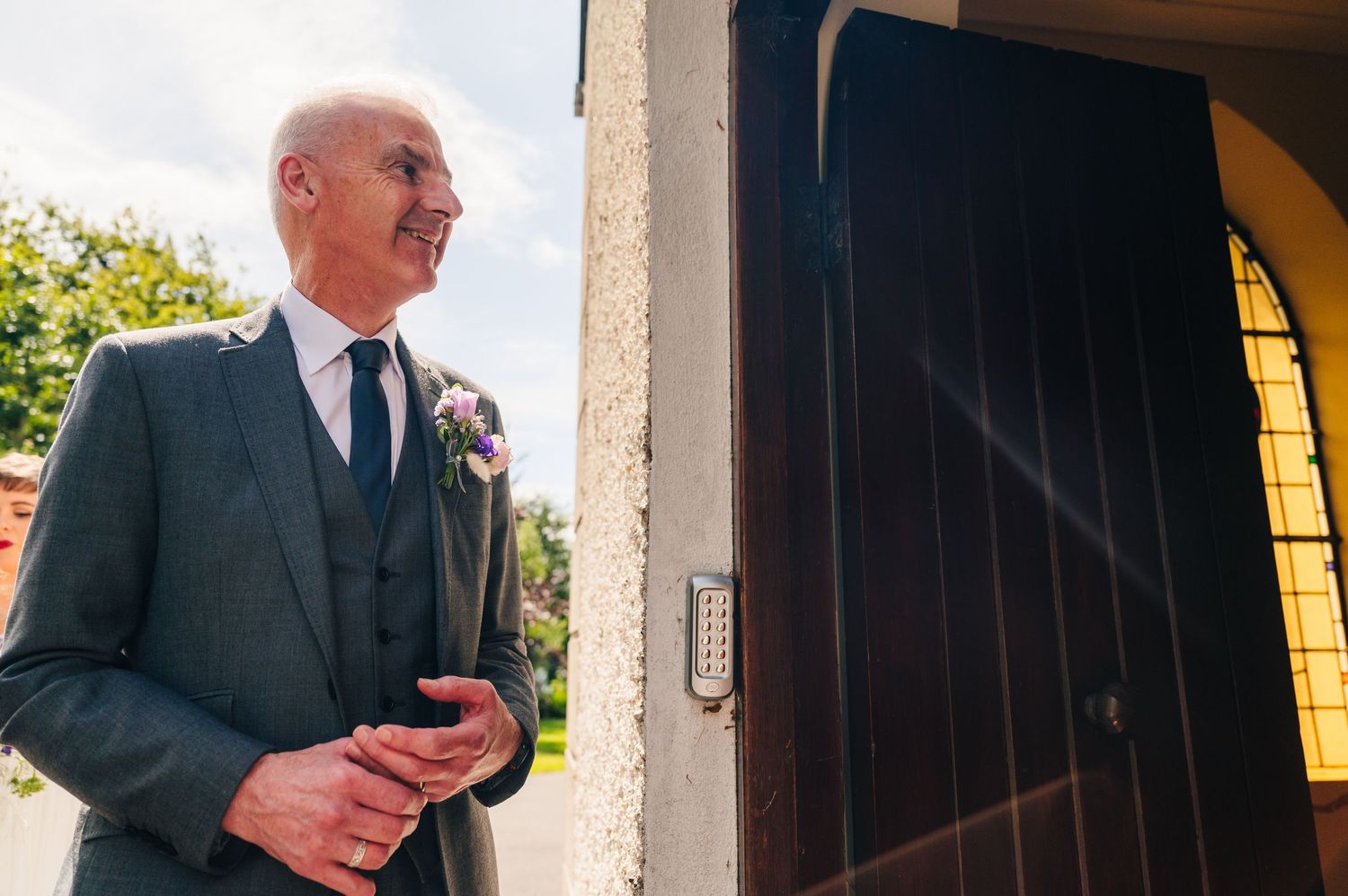 Millhouse slane wedding photographer dublin Formal-dressed man waits pensively outside church doorway in sunlight.