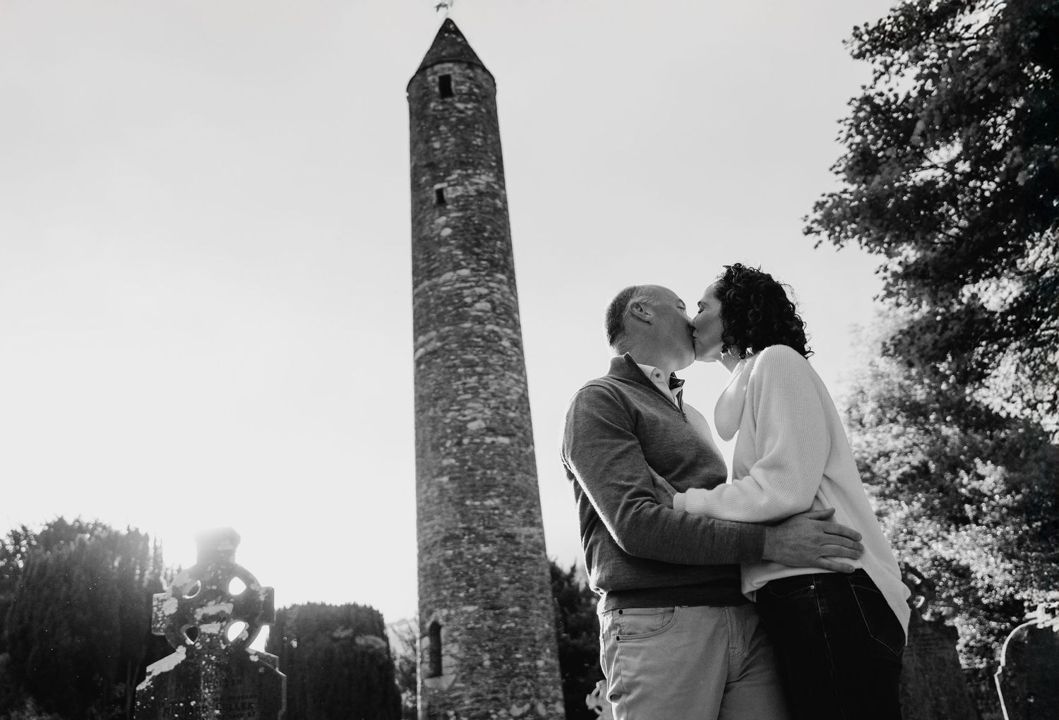 Family photographer Ireland Dublin A romantic black and white moment between a couple in front of a historic stone tower at sunset.