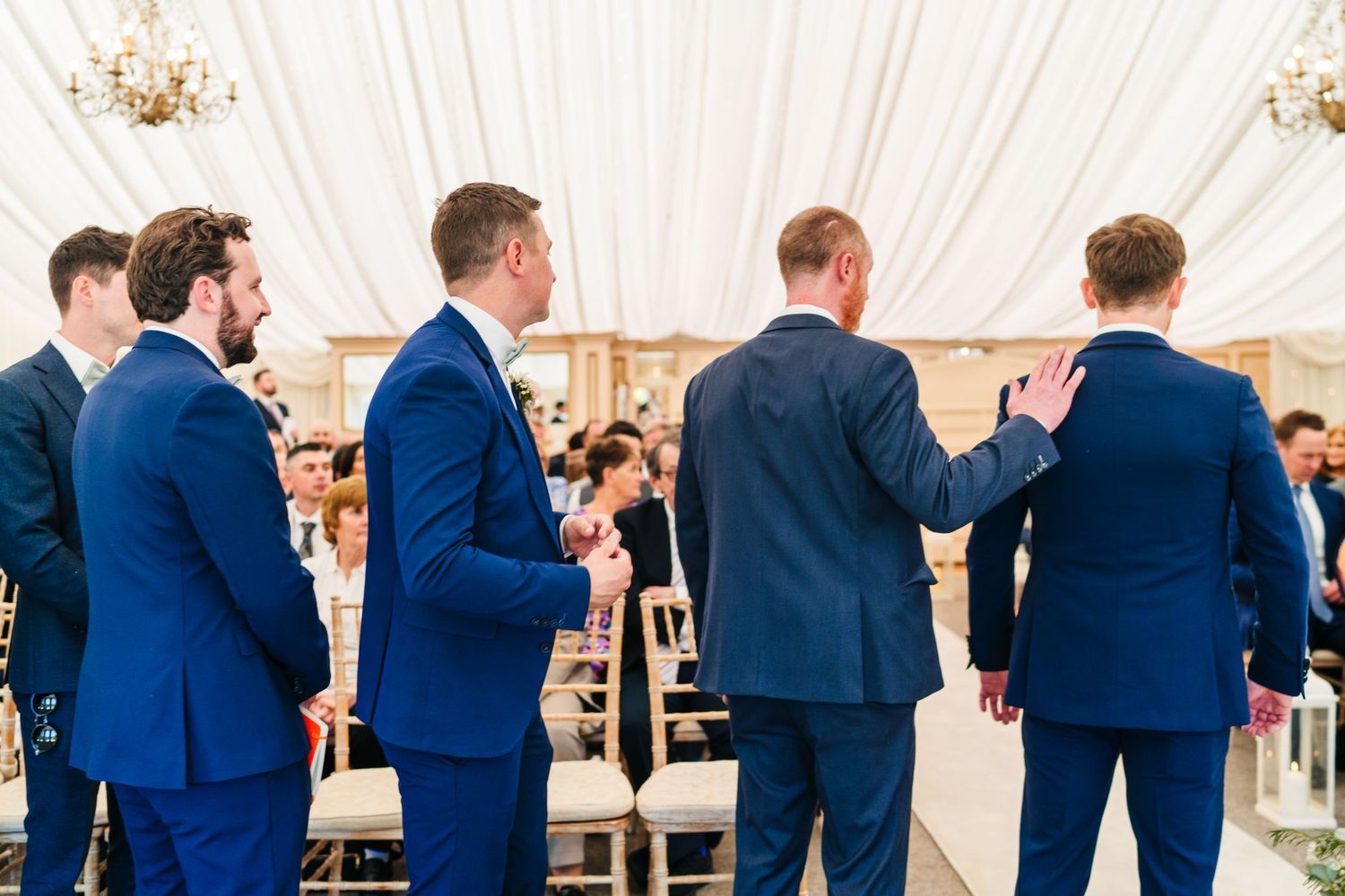 Castle Leslie Wedding Photographer Dublin Groomsmen in matching navy suits stand in a row under white tent at wedding reception.