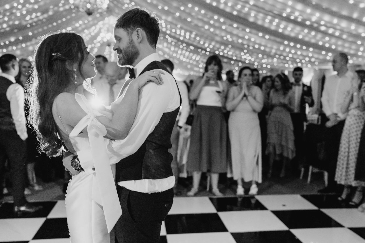 Castle Leslie Wedding PhotographDancing couple surrounded by guests on a checkered dance floor under twinkling lights at wedding reception.