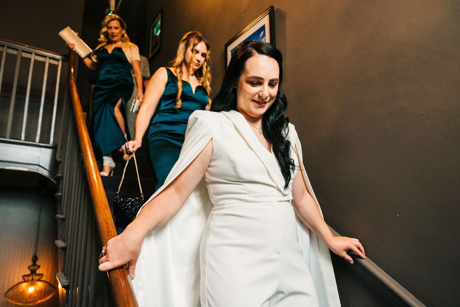 A bride in a white dress descending a staircase with bridesmaids in teal dresses behind her. House Dublin Wedding Photographer