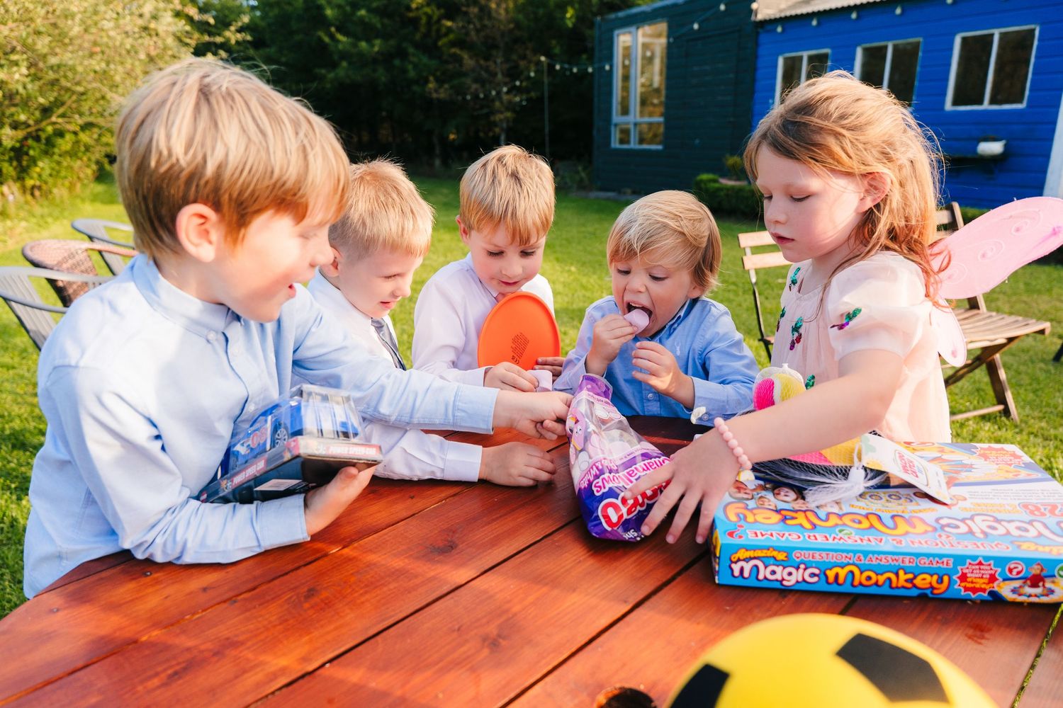 Group of young children playing together at a wooden table outdoors on a sunny day. . Village Barn Tyrrellspass wedding photographer Ireland
