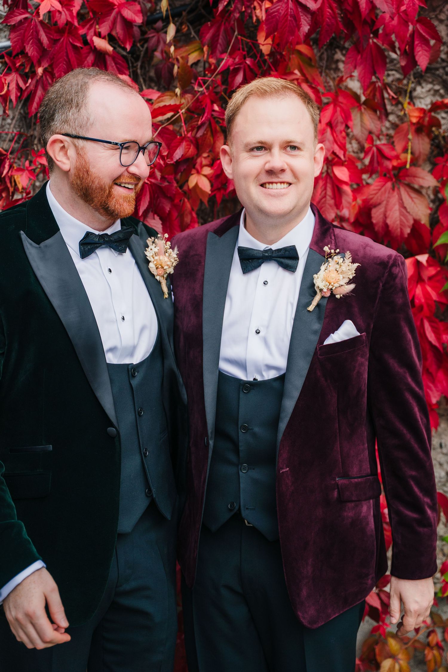 A pair in formal attire pose against a backdrop of vibrant red autumn foliage. LGBTQ Ashley Park Wedding Photographer