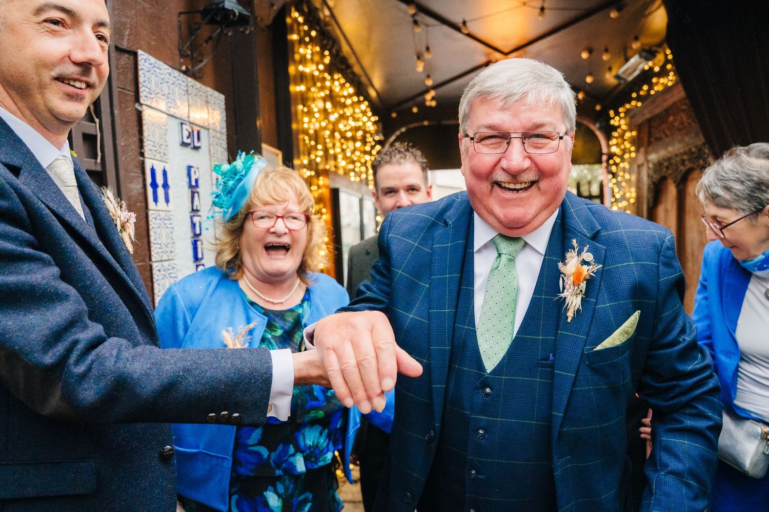 Wedding party members share candid laughs outside venue with decorative lighting. Marco Pierre Dublin Wedding Photographer