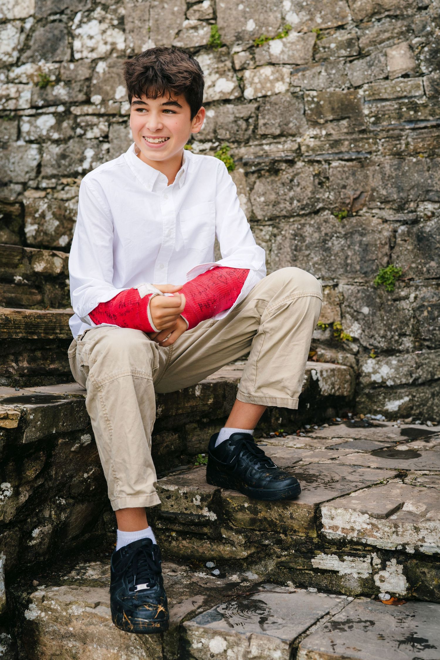 Young person in white shirt and khaki pants sitting on stone steps against an old stone wall. BEctive abbey family photographer dublin