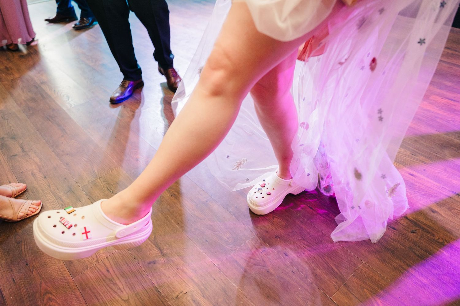 Pink tulle skirt swishes across a wooden dance floor as dancers move in elegant ballroom formation. . Village Barn Tyrrellspass wedding phot