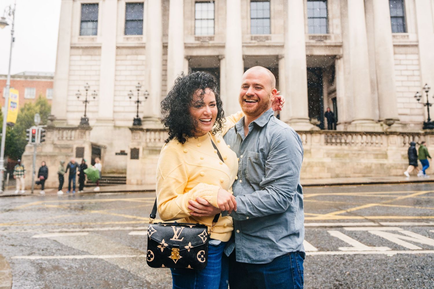 A couple shares joyful moments together during a photo session outside a grand historic building with stone columns. Proposal Dublin Photogr