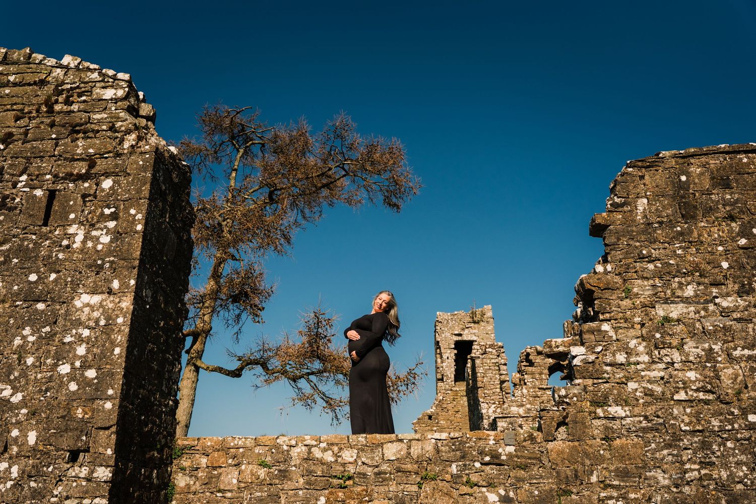 Medieval stone fortress ruins photographed against deep blue sky with tree branches. Family PHOTOGRAPHER Dublin