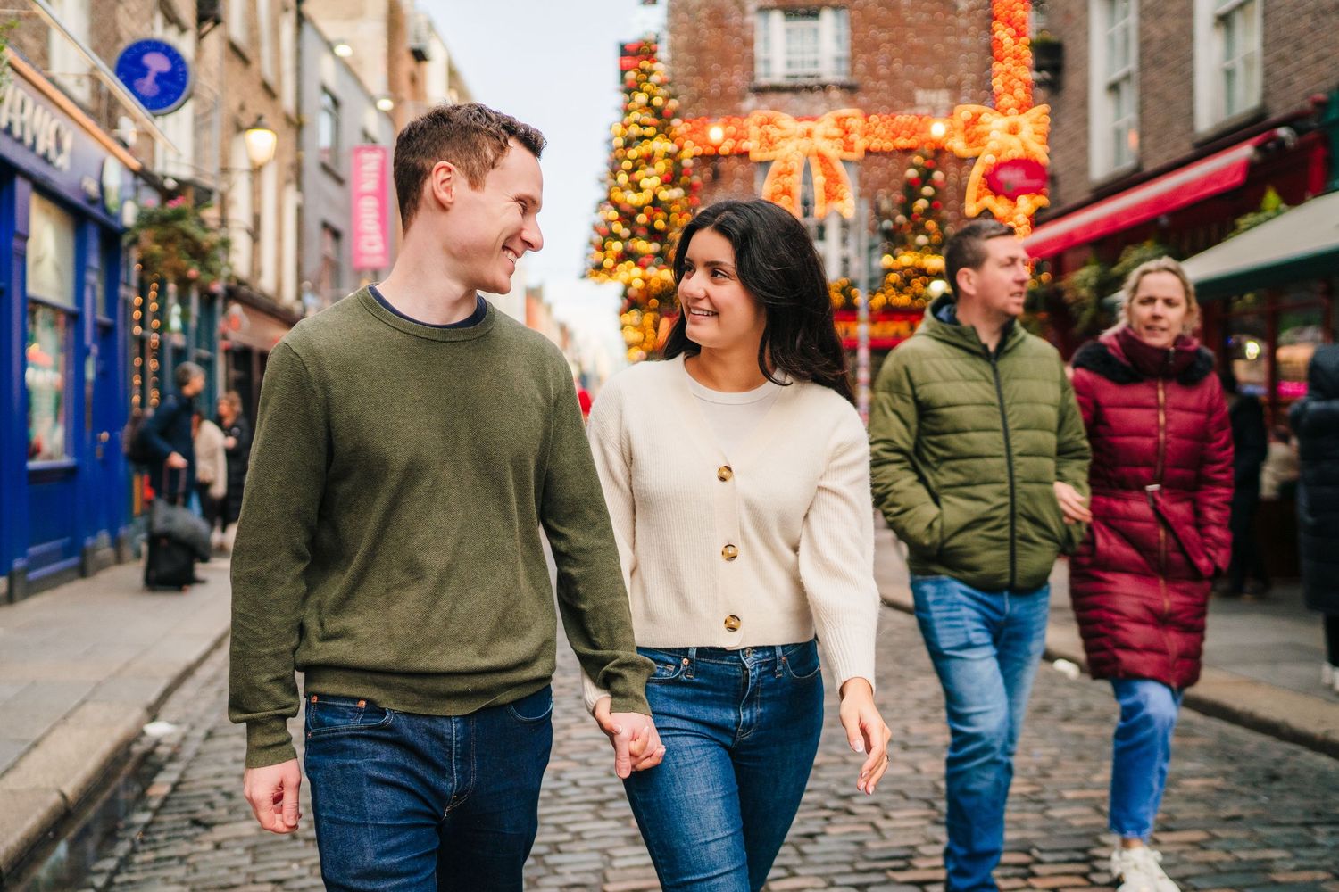 Couple walking and smiling on cobblestone street with autumn decorations and other pedestrians. Surprise proposal dublin photography