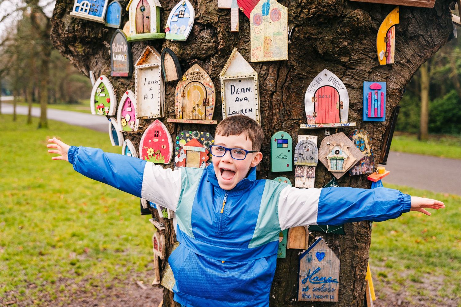 A collection of colorful fairy doors decorating a tree trunk in a grassy park or garden area. Family photographer Dublin Ireland