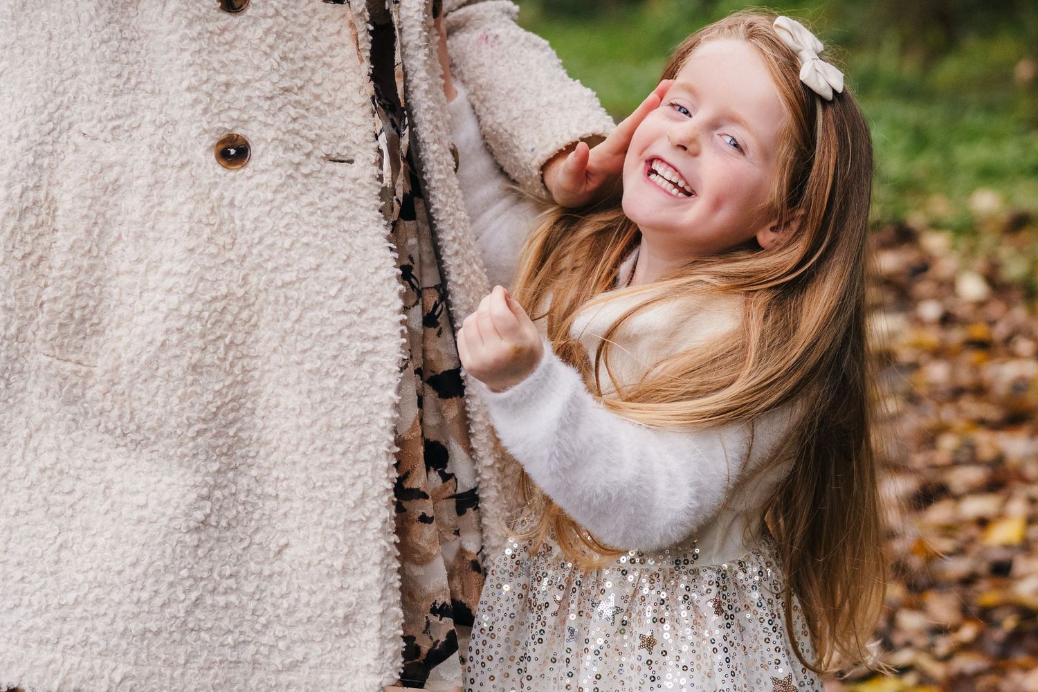 A cheerful person in a cream sweater and sequined skirt poses playfully against a birch tree surrounded by autumn leaves. Family Photographe