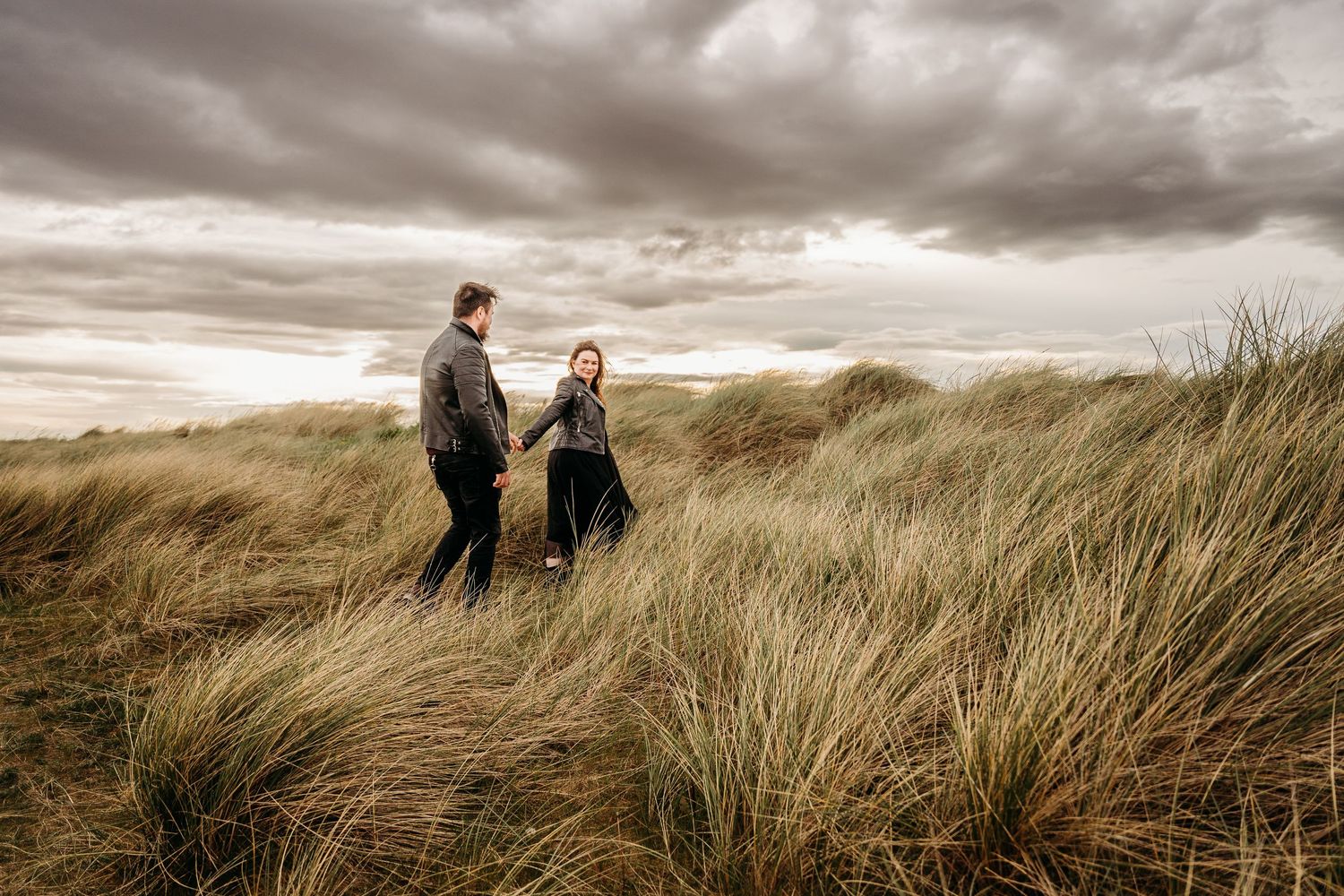 Scenic beach grass landscape with figures silhouetted against stormy skies. engagement PHOTOGRAPHER Dublin