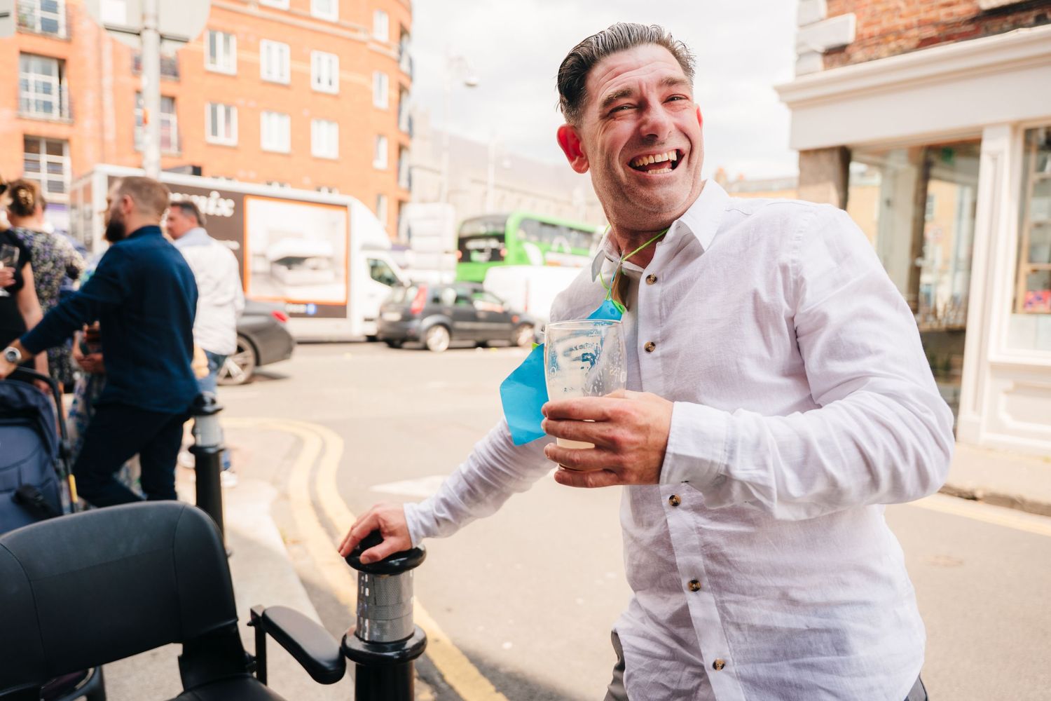 Person in white shirt laughs while holding a blue drink outdoors. Same sex wedding PHOTOGRAPHER Dublin