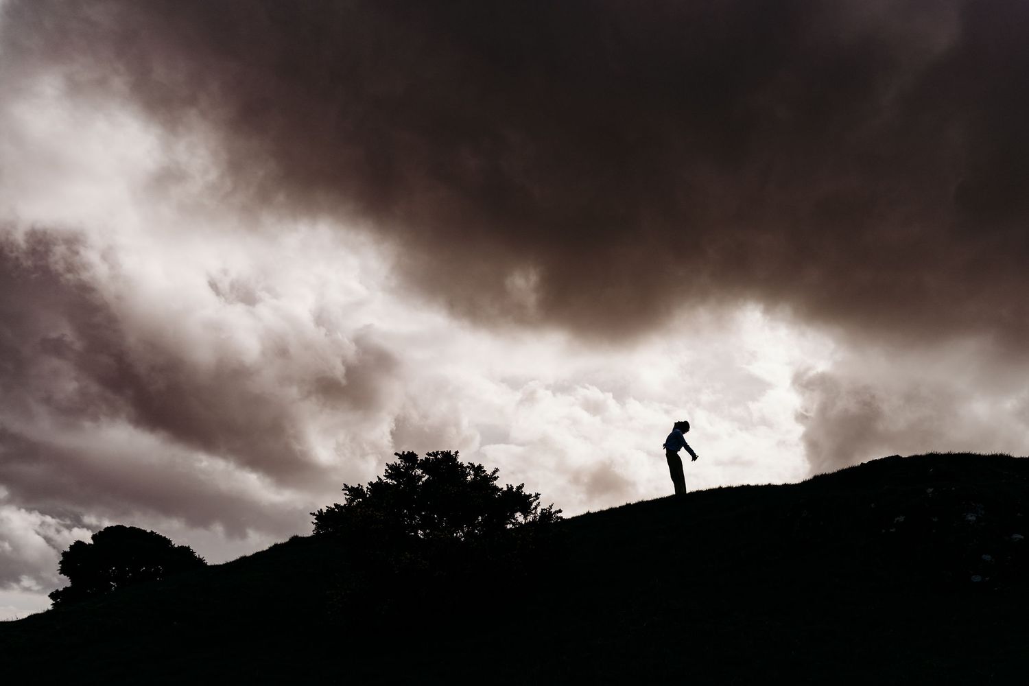 Portrait PHOTOGRAPHER Dublin A silhouetted figure stands atop a hill against dramatic storm clouds in a moody black and white landscape.