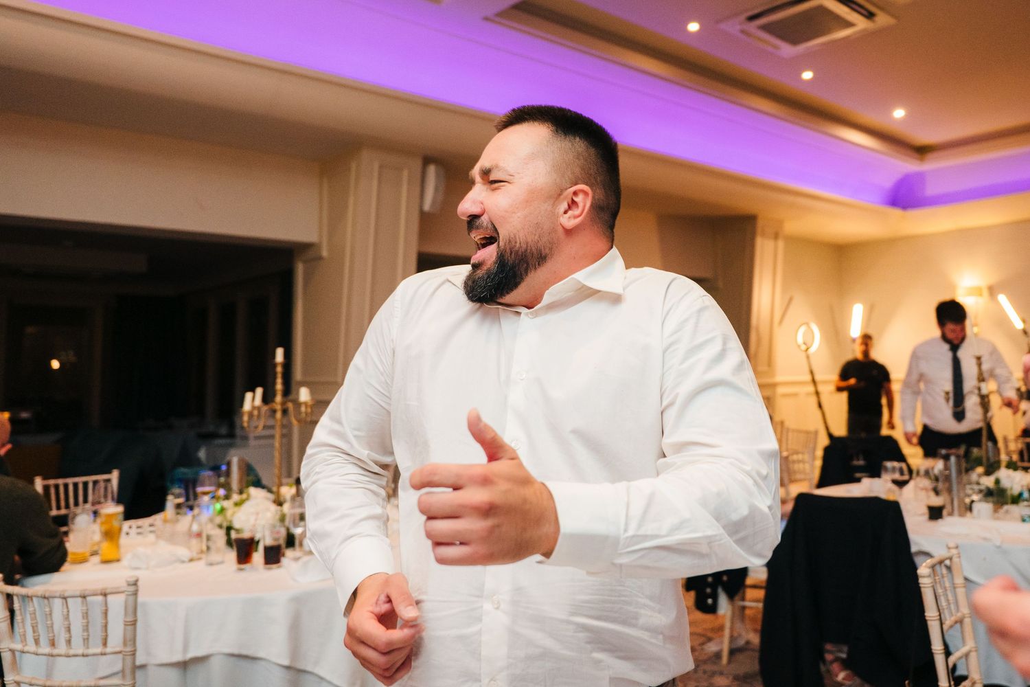 A person in a white dress shirt gestures expressively during a wedding reception. Portmarnock Hotel Wedding PHOTOGRAPHER Dublin