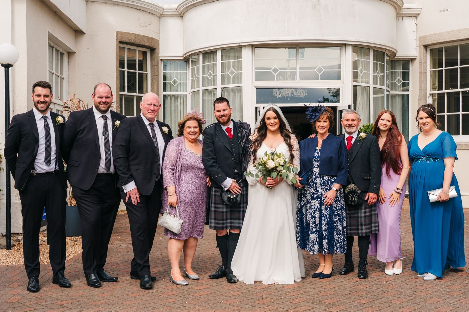 Wedding party members pose together outside an elegant white building for a formal group photo. Portmarnock Hotel Wedding PHOTOGRAPHER Dubli