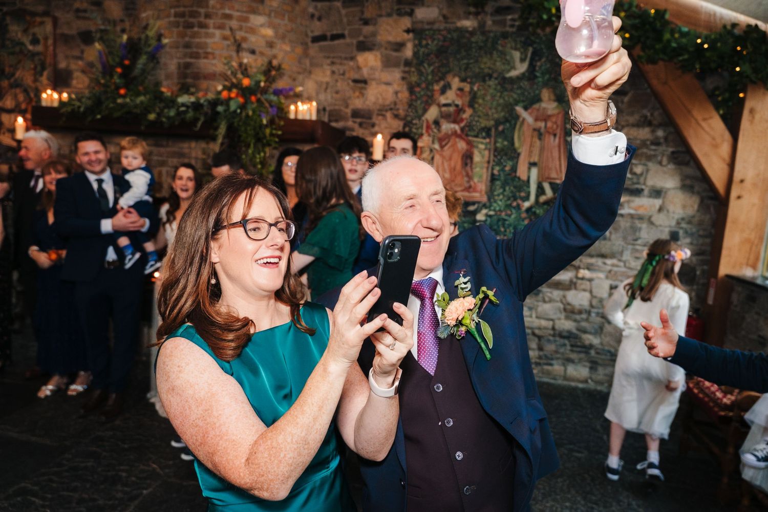 Wedding party celebrating and dancing together inside a rustic brick-walled venue with warm lighting.
