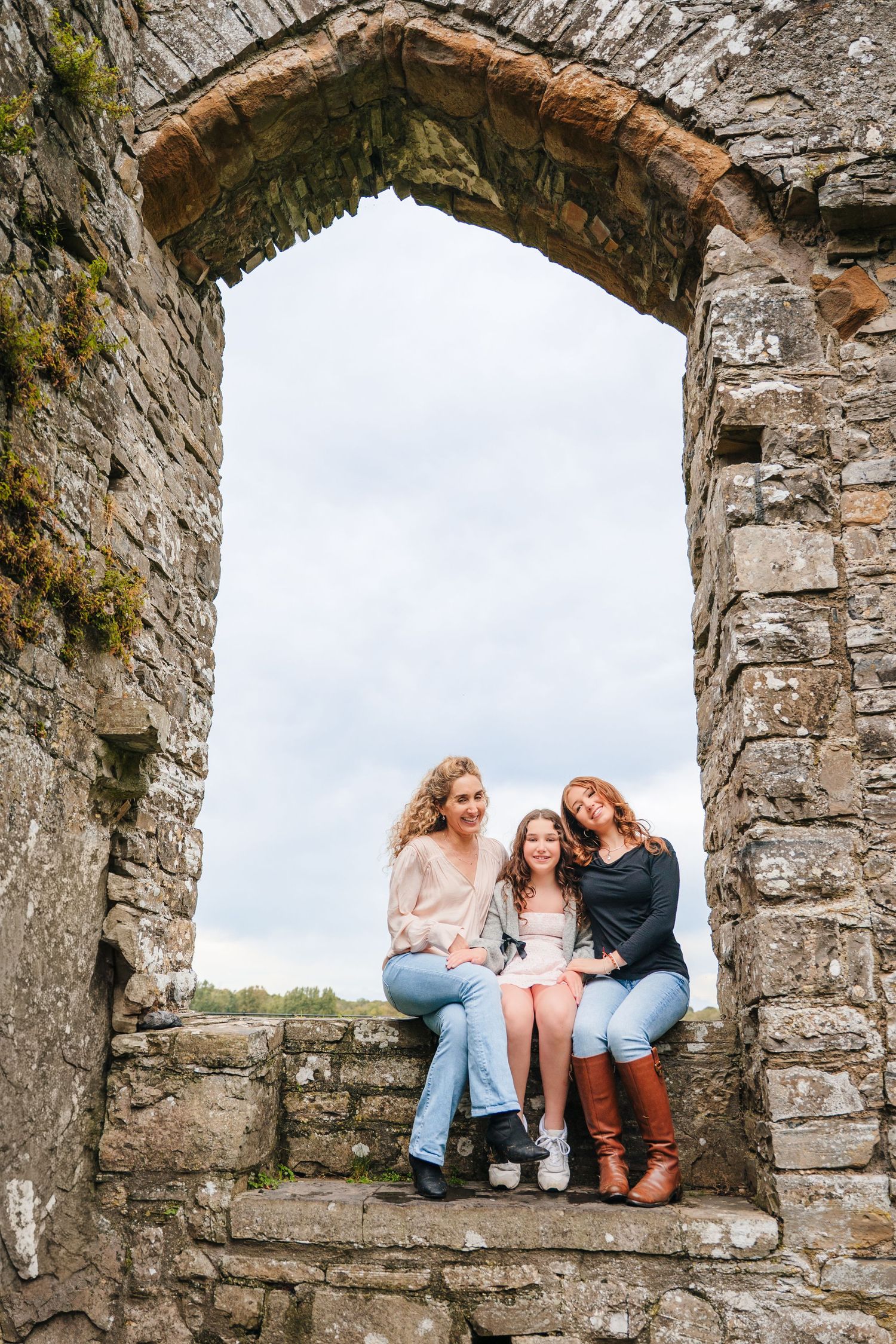 Friends sharing laughs while sitting in stone archway windows of historic ruins. BEctive abbey family photographer dublin