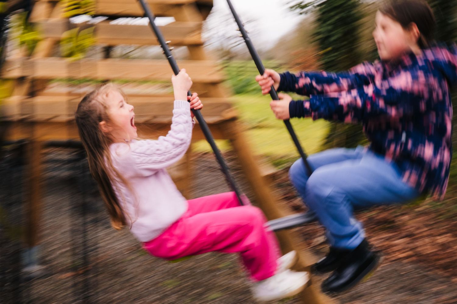 Two children play on swings in motion creating a blurred action shot effect outdoors. family PHOTOGRAPHER Dublin