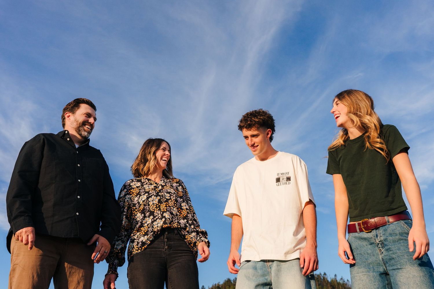 A group of people stand against a vibrant blue sky background on a sunny day in a casual gathering. family PHOTOGRAPHER Dublin