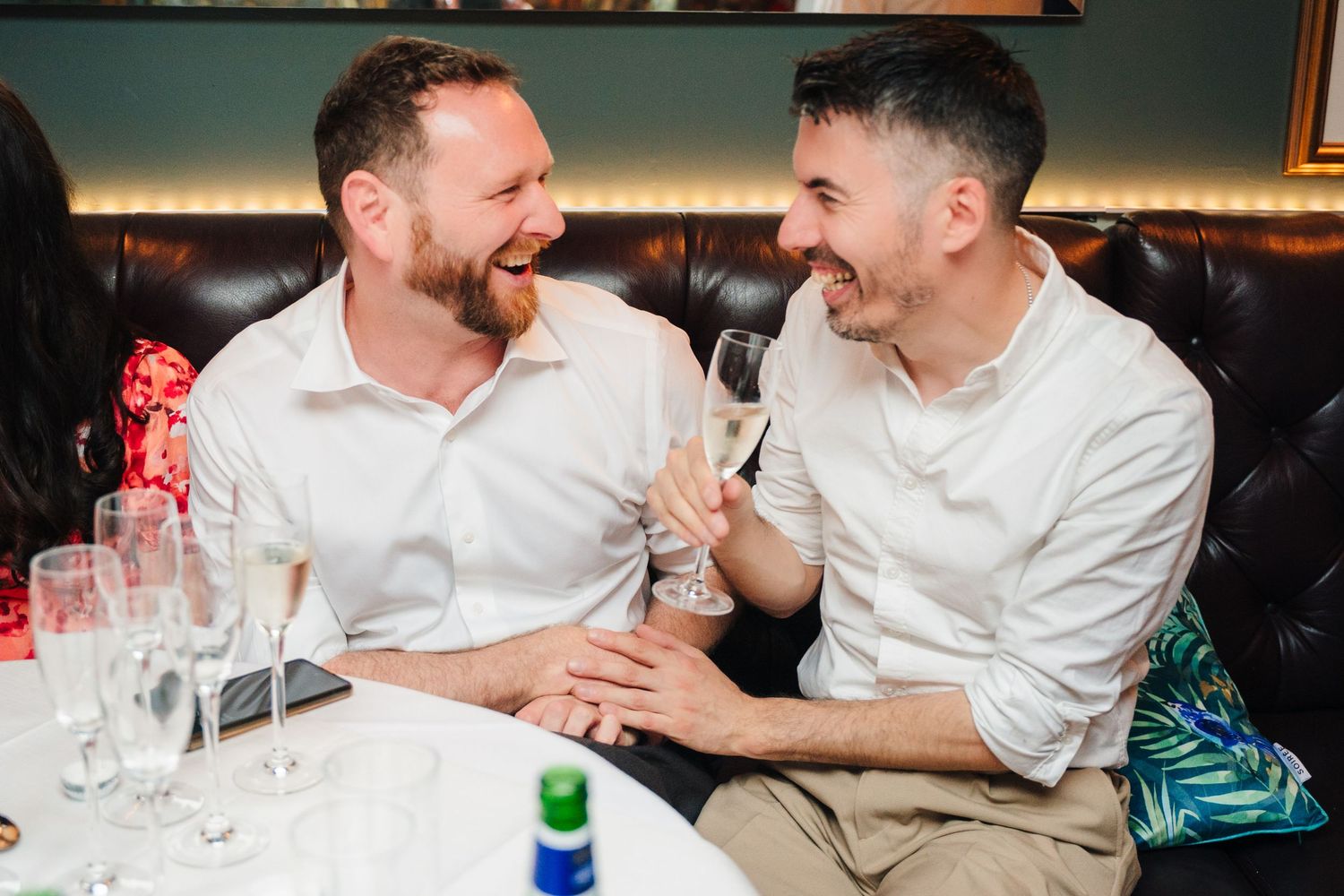 Two people share a candid laughing moment while seated at a dining table. Marco Pierre Dublin Wedding Photographer