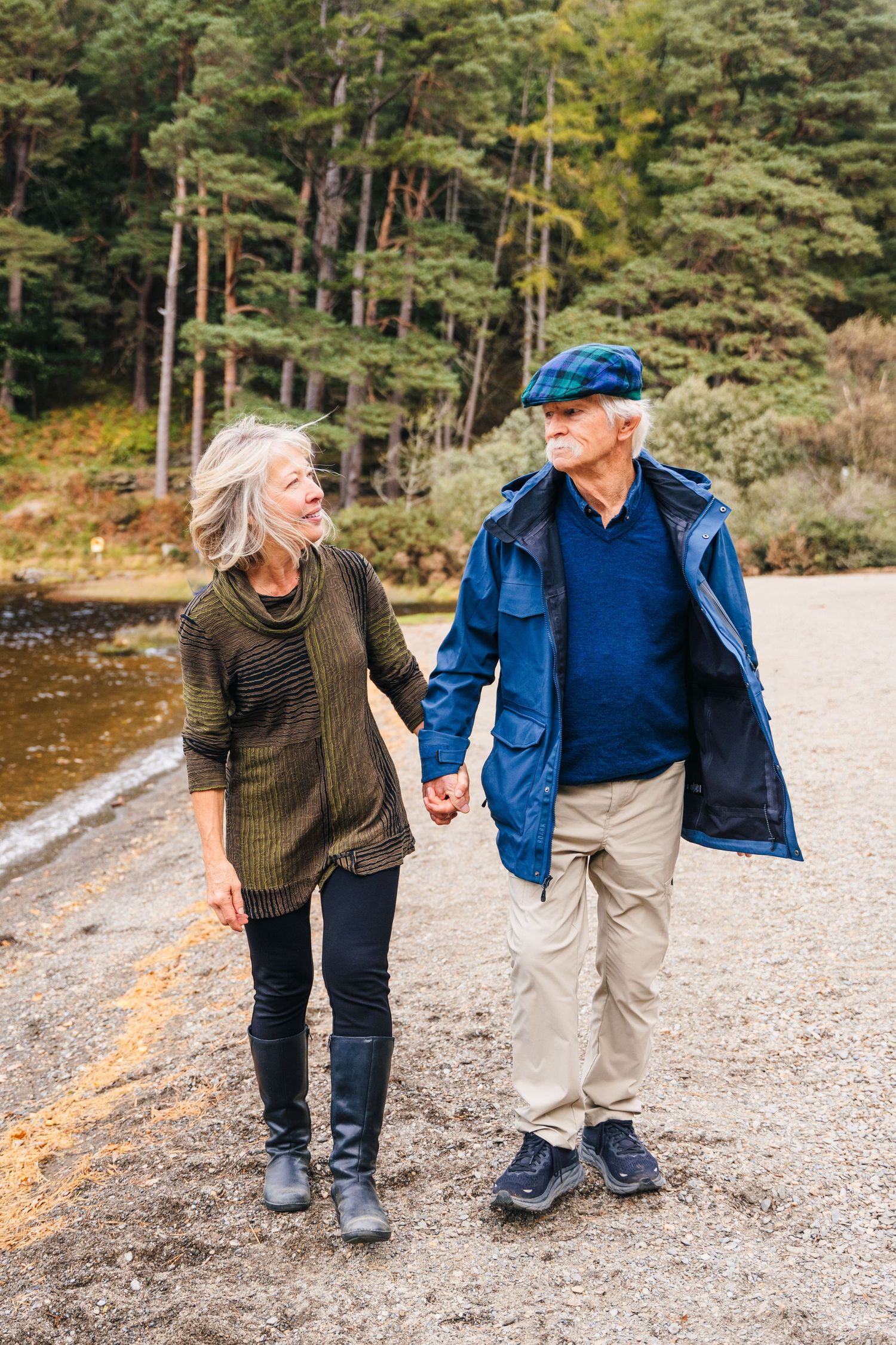 People walking and laughing together along a rocky shoreline surrounded by pine trees and mountains.Family photogrAPHER DUBLIN