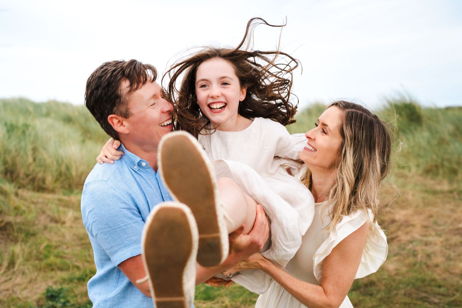 A playful family moment captured outdoors with everyone laughing and having fun in a natural setting.  Family photographer Dublin Ireland