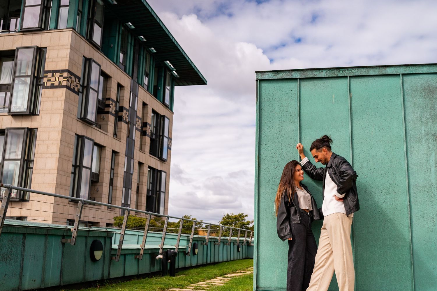 People pose playfully in front of a modern green building with cloudy sky above. couple's photographer photoshoot Dublin Ireland