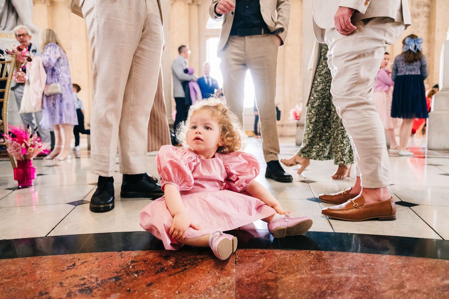 Young child in pink dress playing on marble floor during wedding celebration.  city hall dublin wedding photos