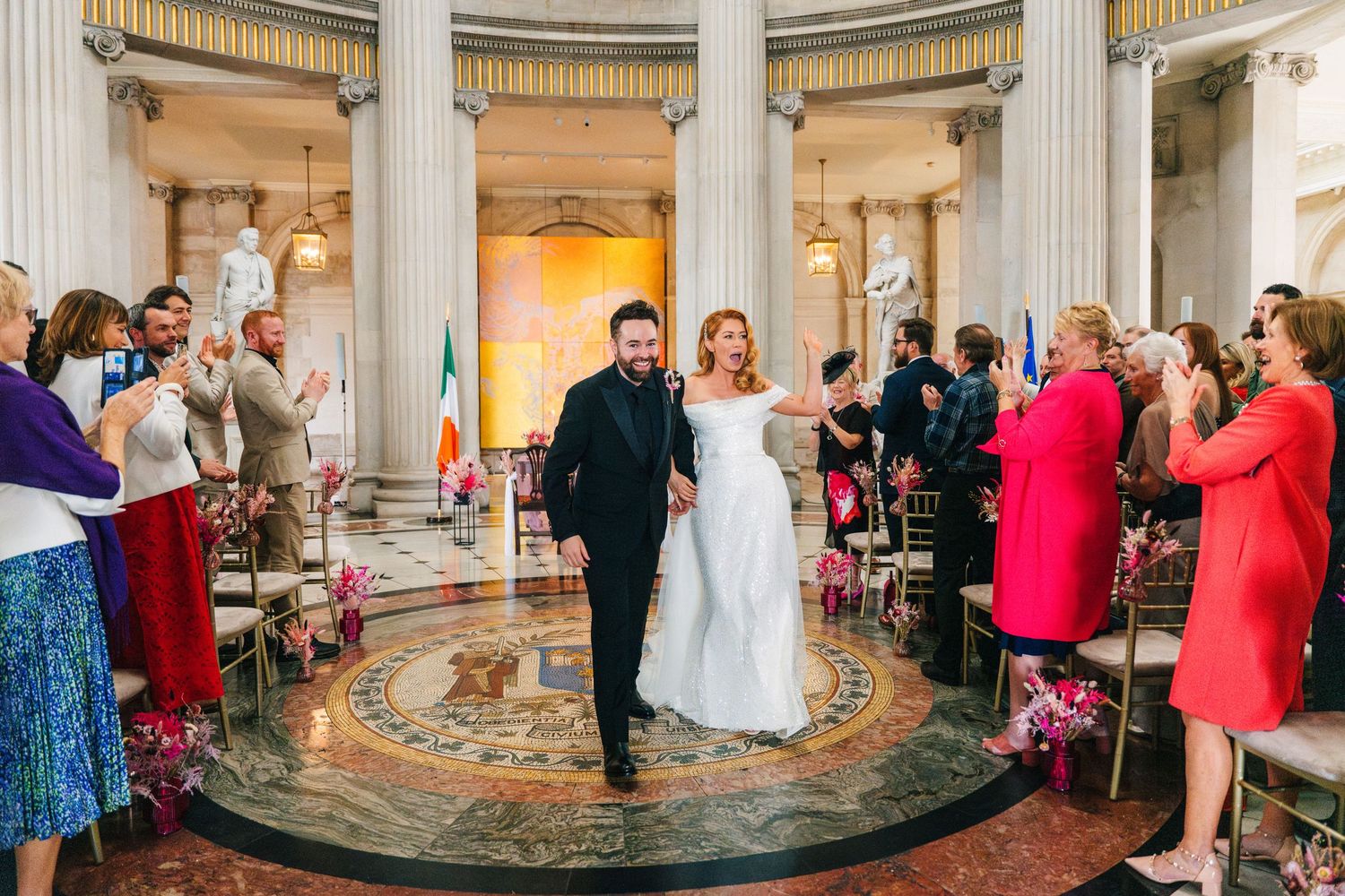 Wedding guests dance and celebrate during a reception in an elegant ballroom with ornate columns and circular architecture.  city hall dubli