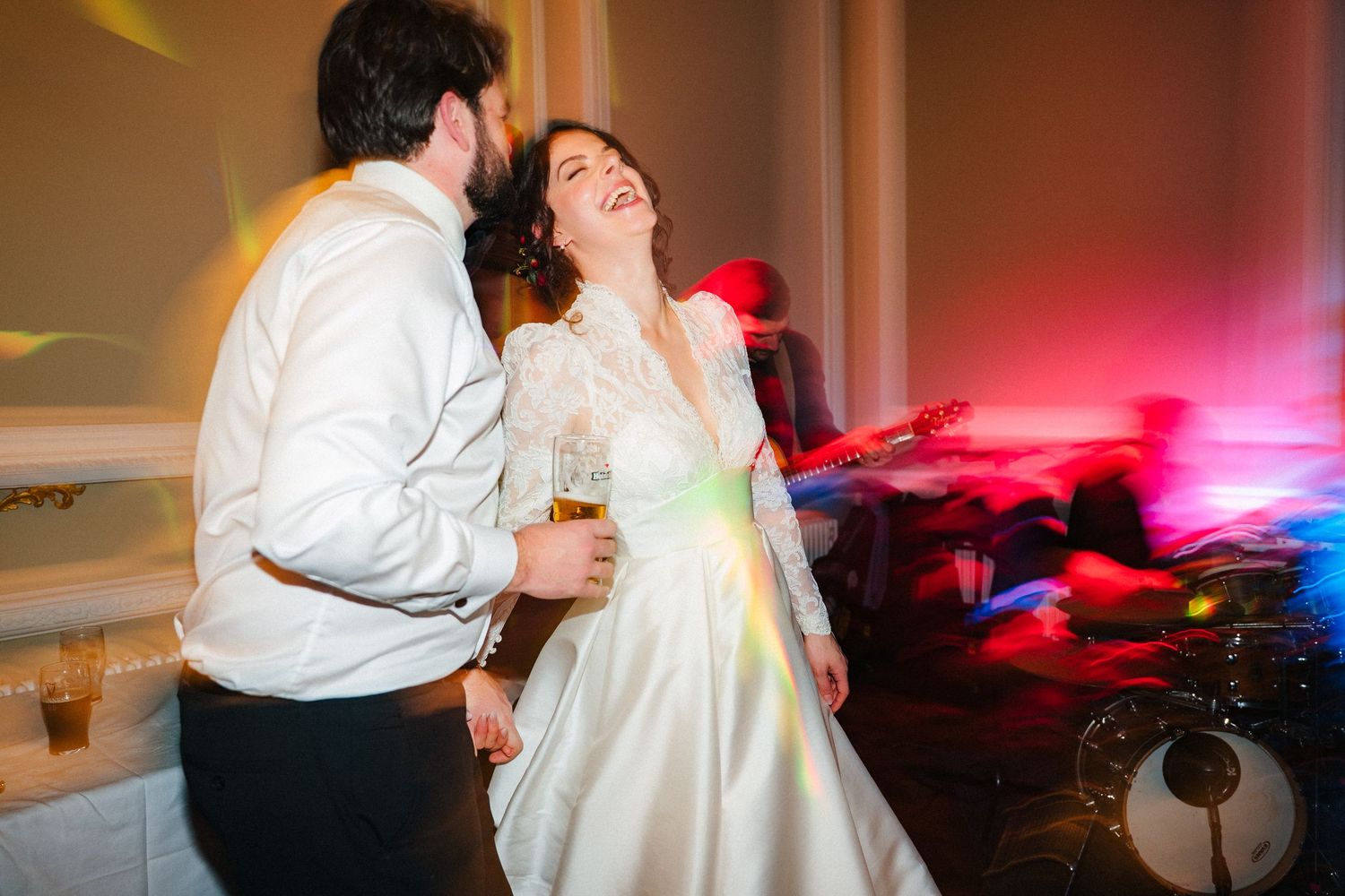 Couple dancing together at a wedding reception with red and blue lighting effects in the background.