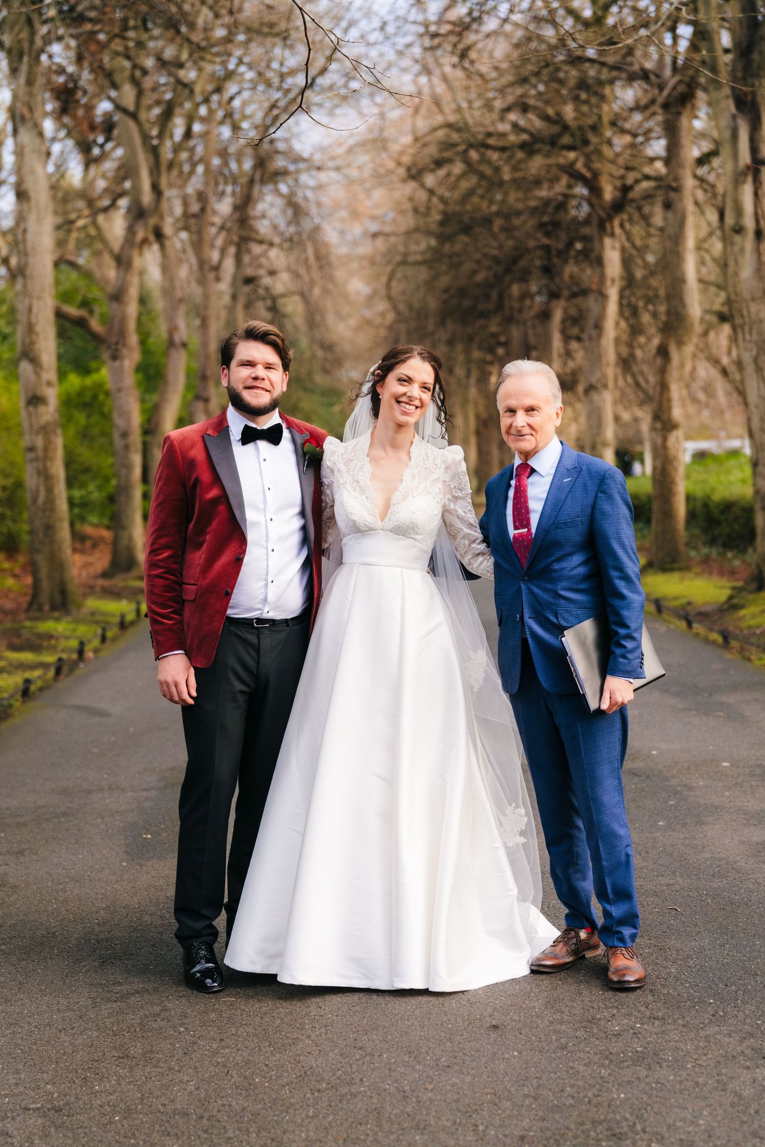 Wedding party poses creatively on tree-lined path in formal attire during autumn photoshoot. Stephens green club dublin Wedding photographer