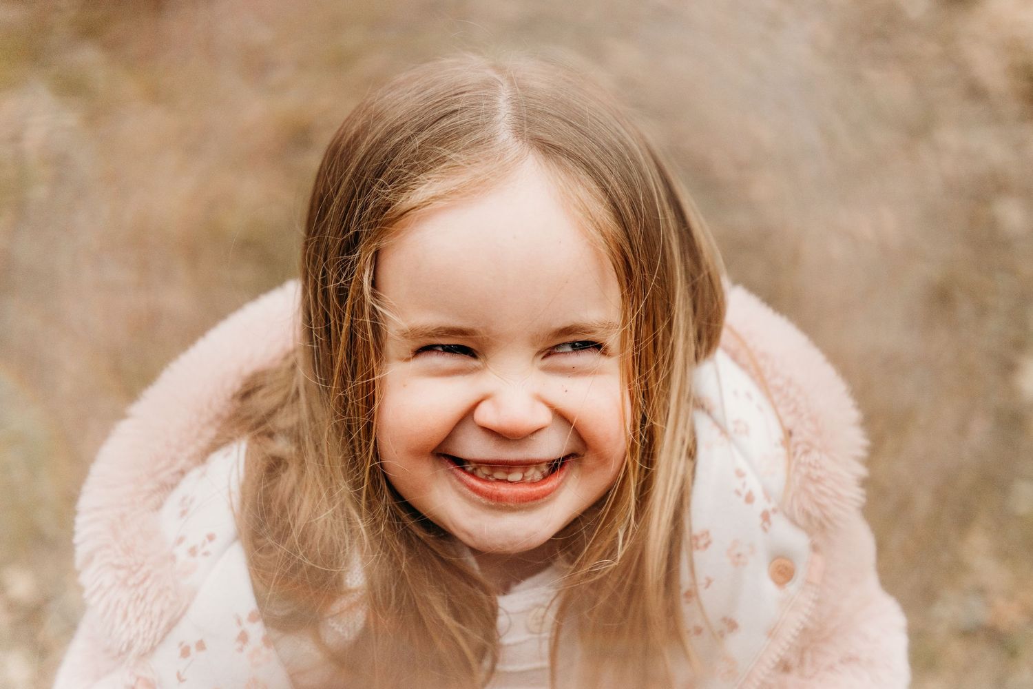 A joyful child wearing a cozy pink winter coat smiles brightly against a blurred brown background.Family photographer Dublin Ireland