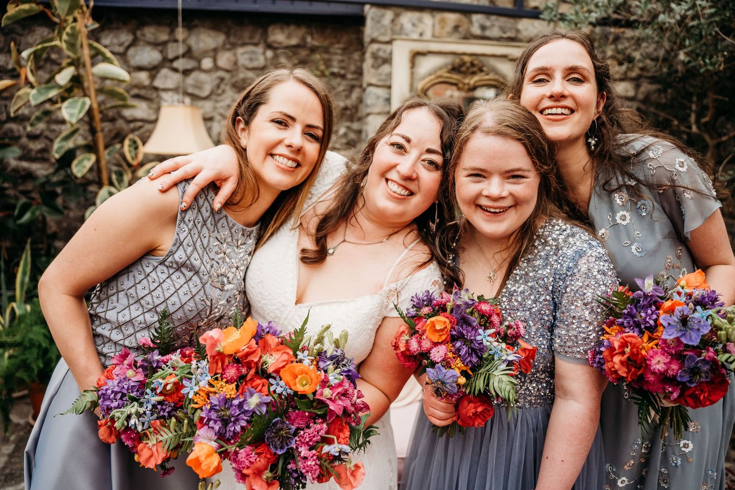 Wedding party members pose with vibrant red and blue floral bouquets. Wedding photographer Dublin