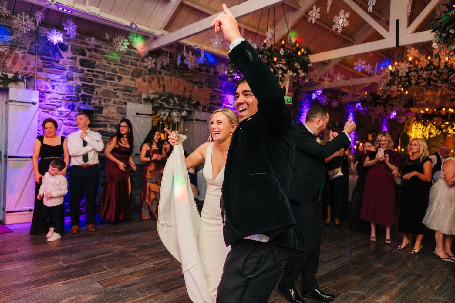 Wedding party dances under wooden beams with purple lighting and festive decorations. Ballymagarvey Wedding photographer