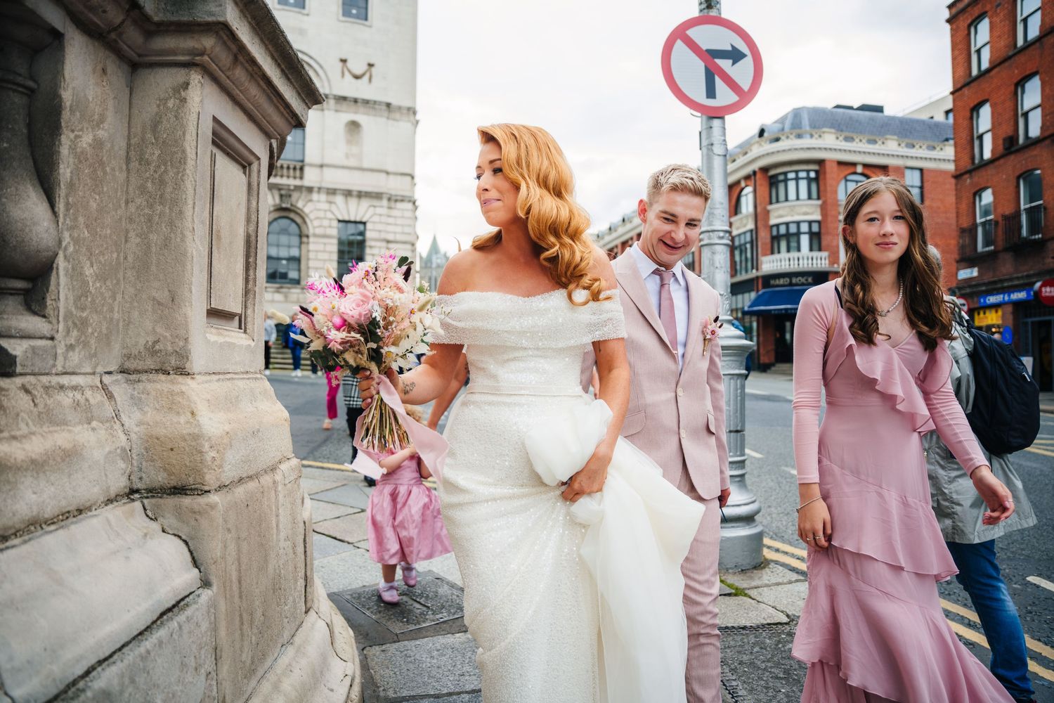 Wedding party celebrating on a city street with joyful expressions and pink floral details.  city hall dublin wedding photos