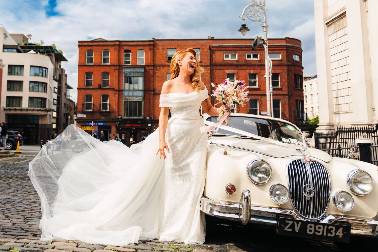 Classic white wedding car parked in front of historic red brick buildings under blue sky.  city hall dublin wedding photos