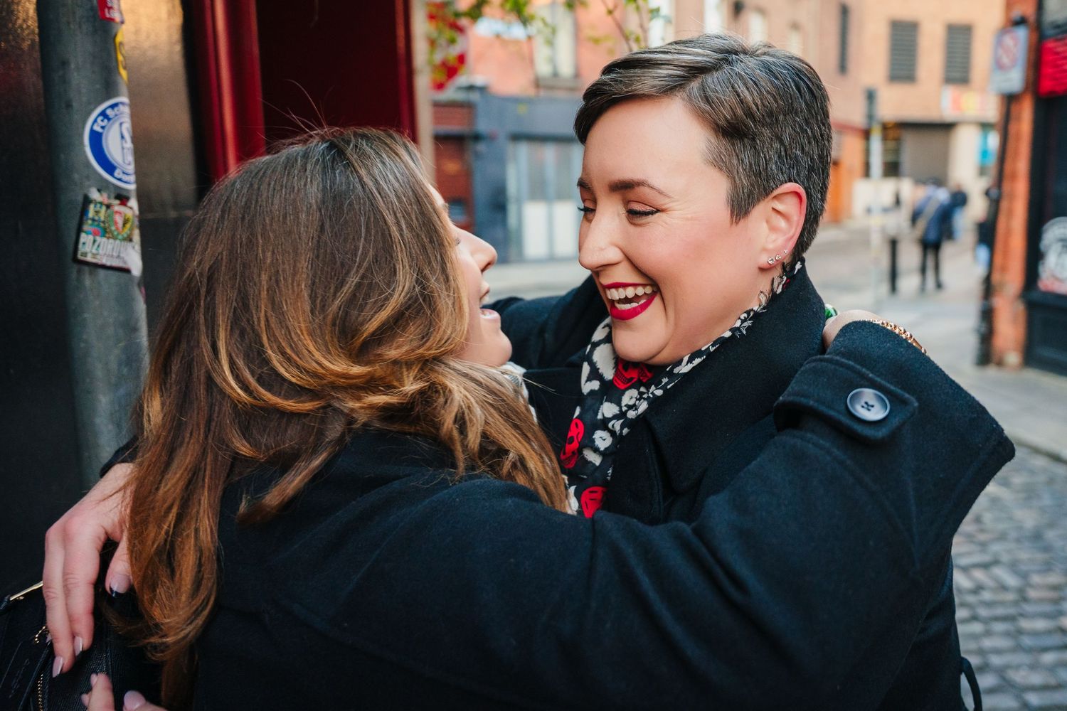 Two people in black coats share a joyful moment while embracing on a cobblestone street. Family walking through Dublin city centre during a