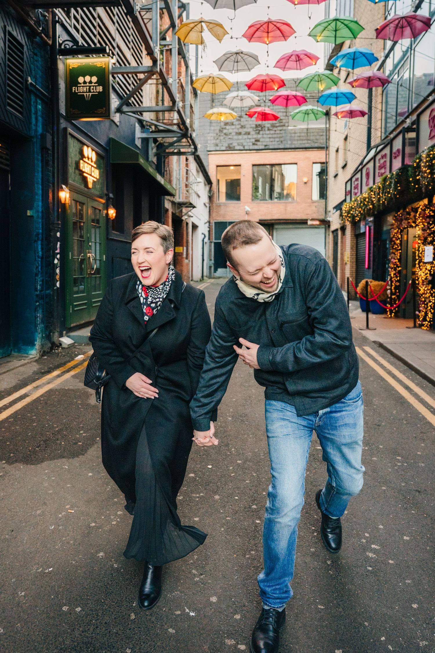 A series of candid photos showing two people laughing together under colorful umbrellas on a charming city street. family PHOTOGRAPHER Dubli