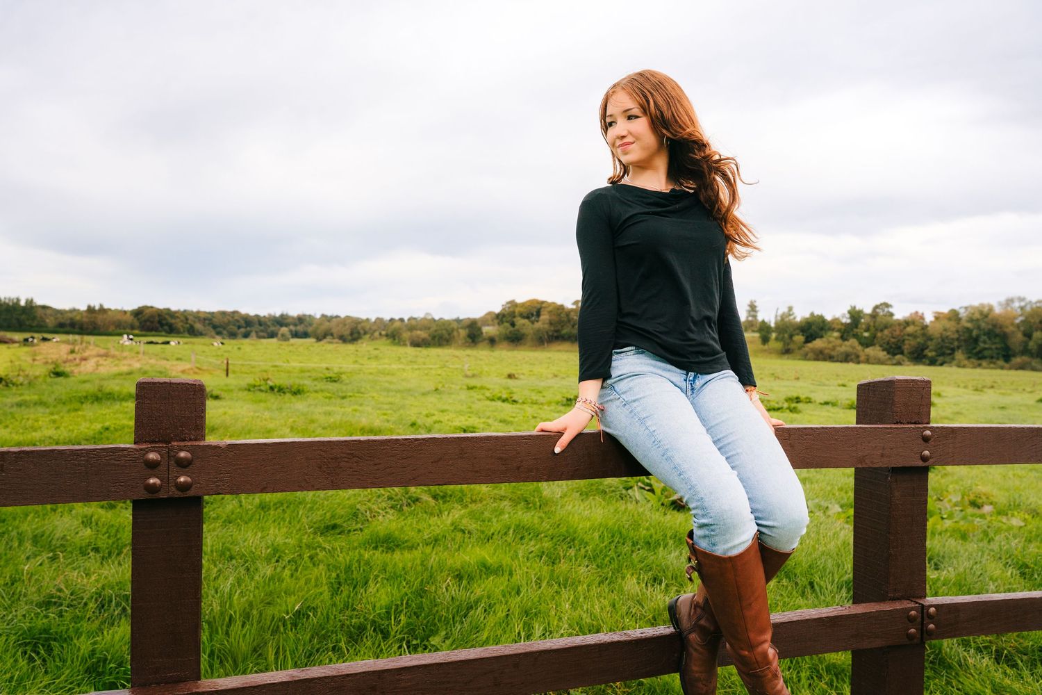 Person sitting on wooden fence overlooking green pastoral countryside. BEctive abbey family photographer dublin