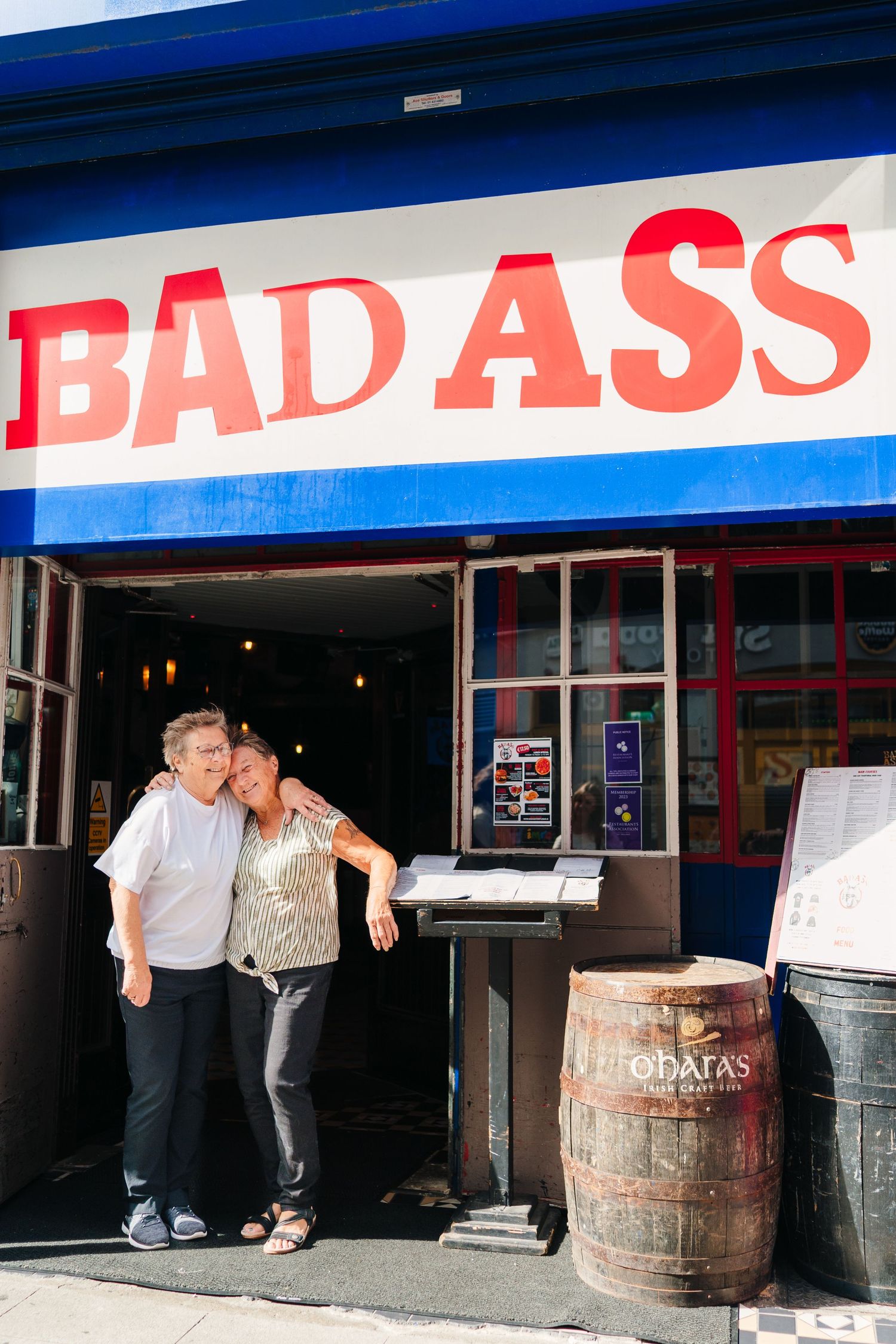 A storefront with wooden barrels outside shows a red sign reading 'BAD ASS' in capital letters. Family photographer Dublin Ireland