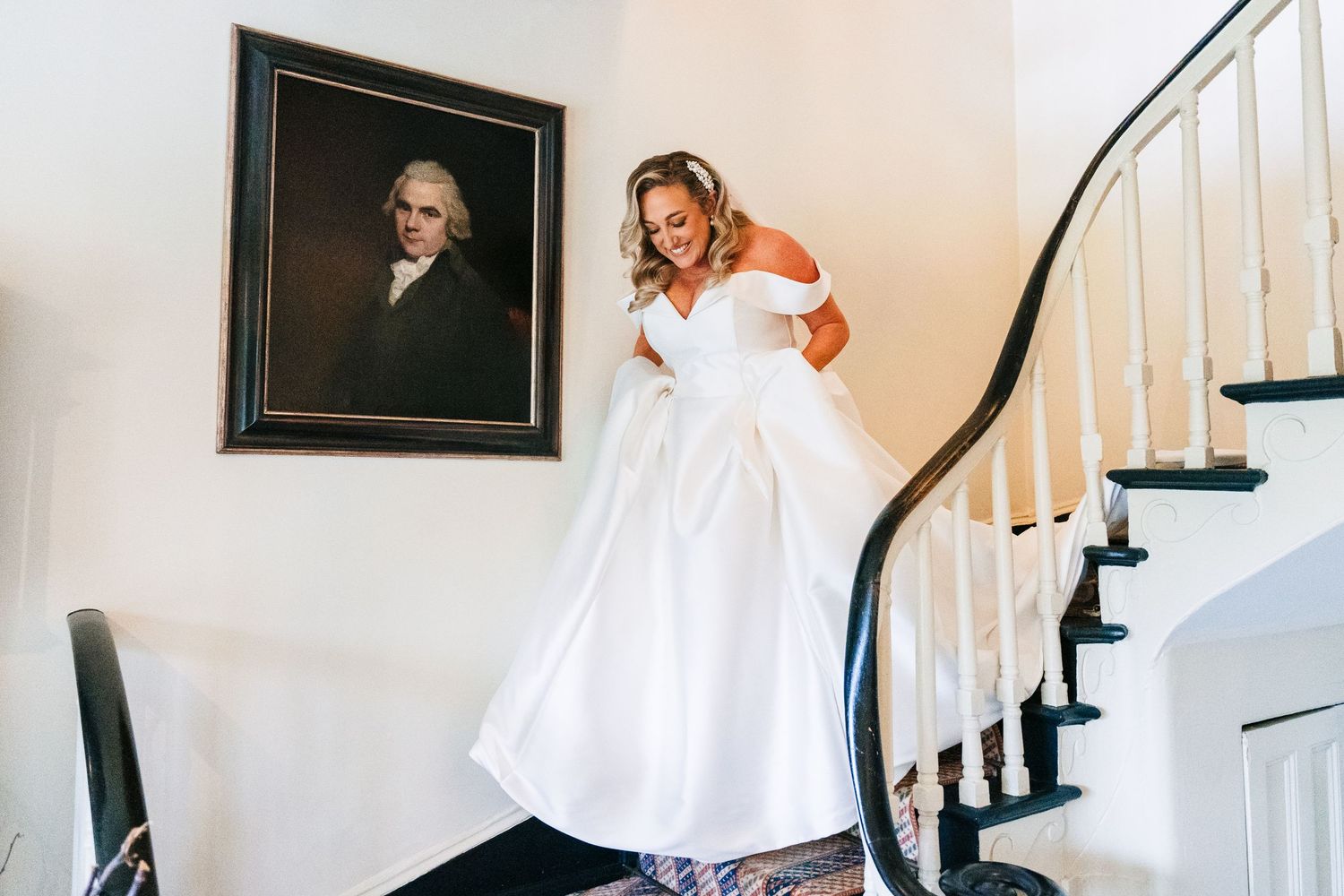 A bride in a white off-shoulder wedding dress poses dramatically on an elegant curved staircase. Virginia Park Lodge Wedding Photographer Du