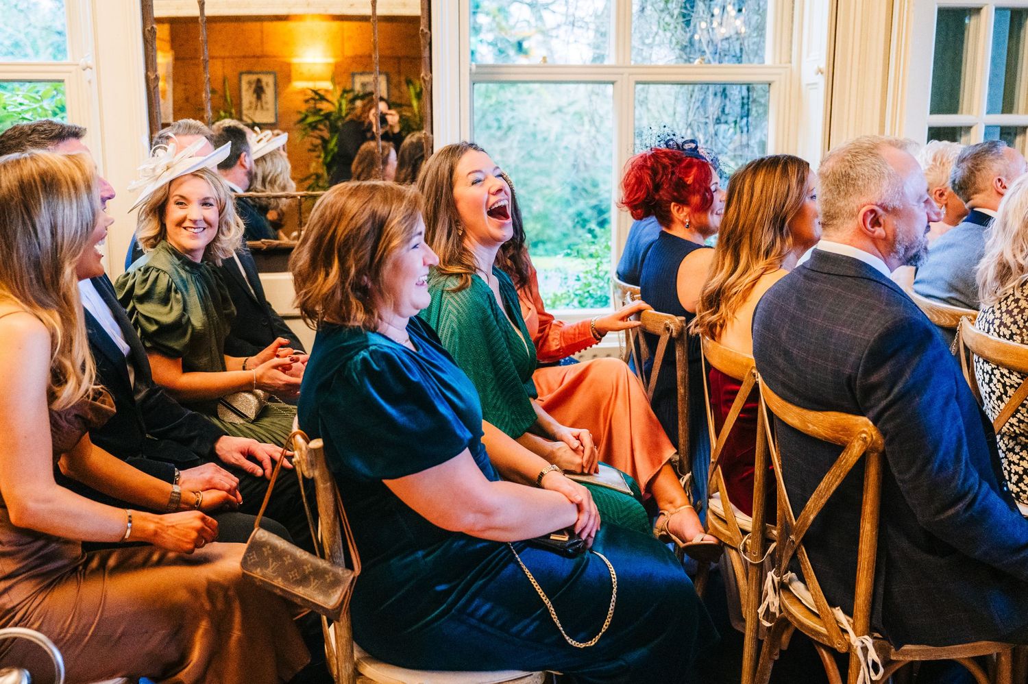 Wedding reception guests enjoying lively conversations and laughter at wooden chairs.  Virginia Park Lodge Wedding Photographer Cavan Dublin