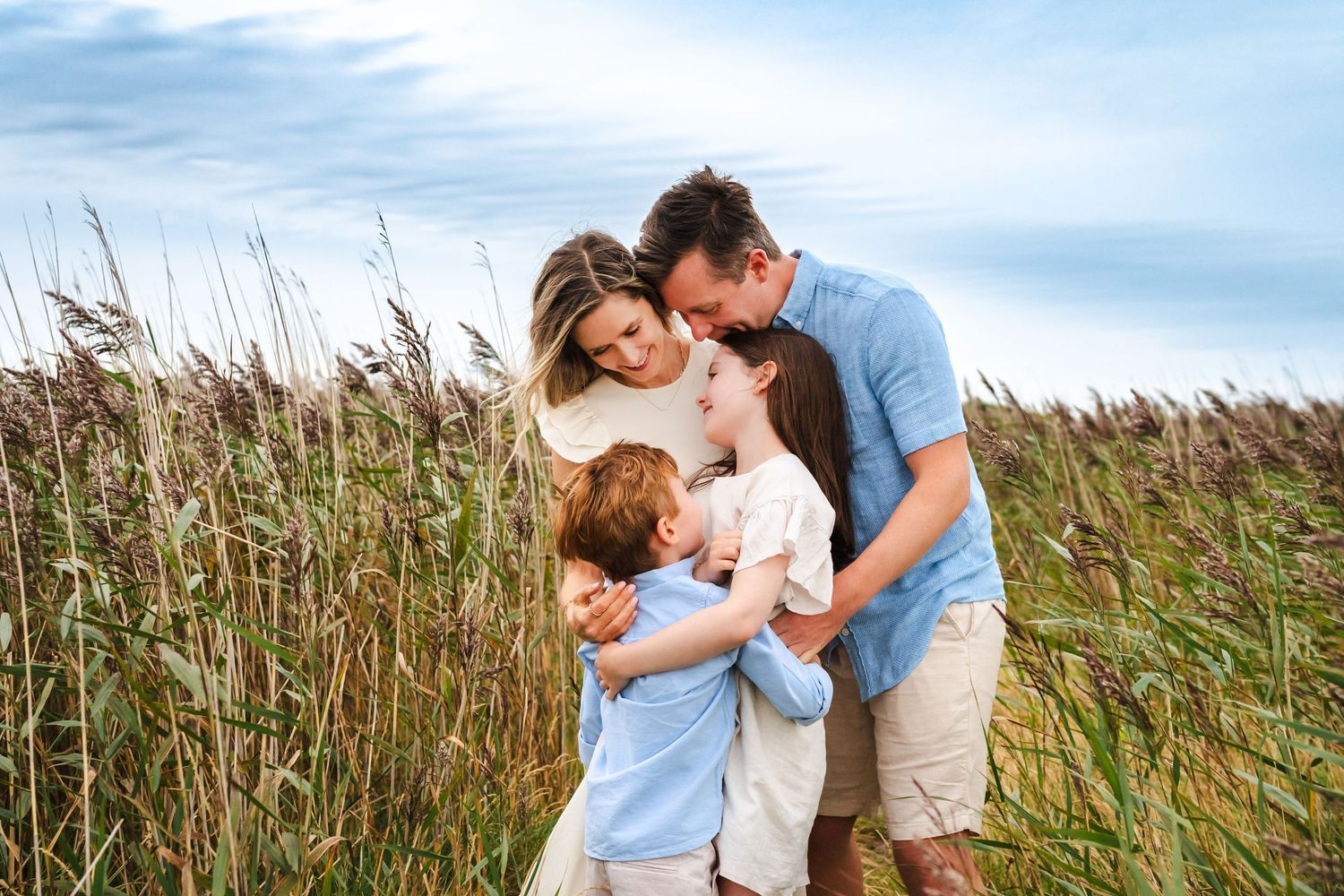 Family shares tender moments together in a field of tall grass during sunset photo session.  Family photographer Dublin Ireland