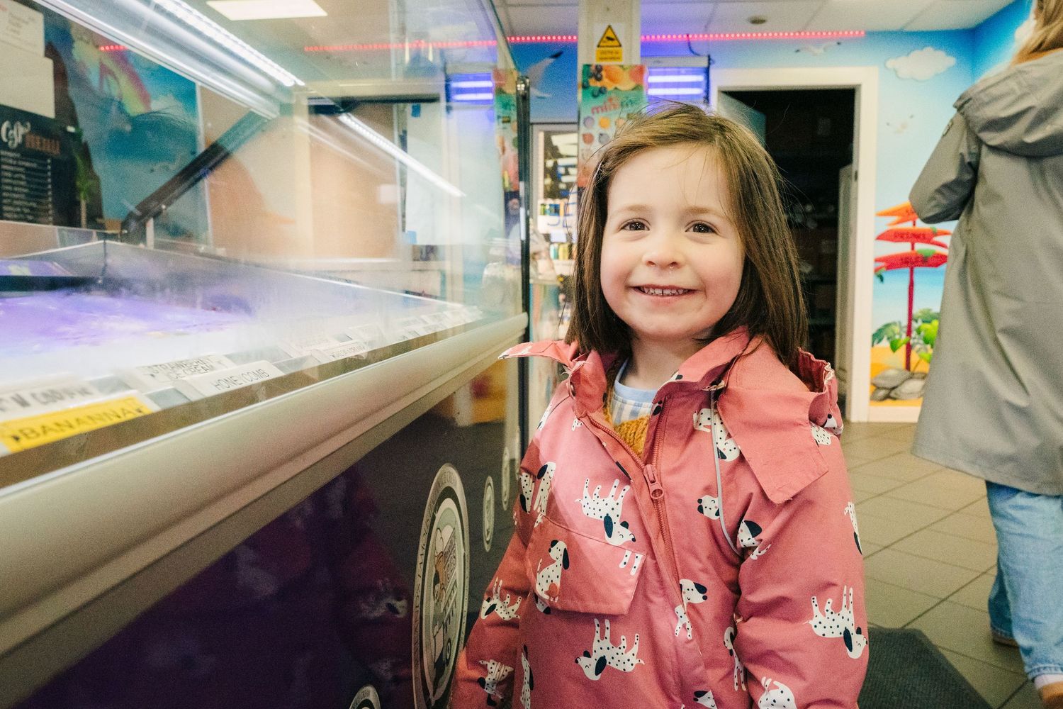 A young person in a pink patterned coat smiles while standing next to an ice cream truck counter. PHOTOGRAPHER Dublin