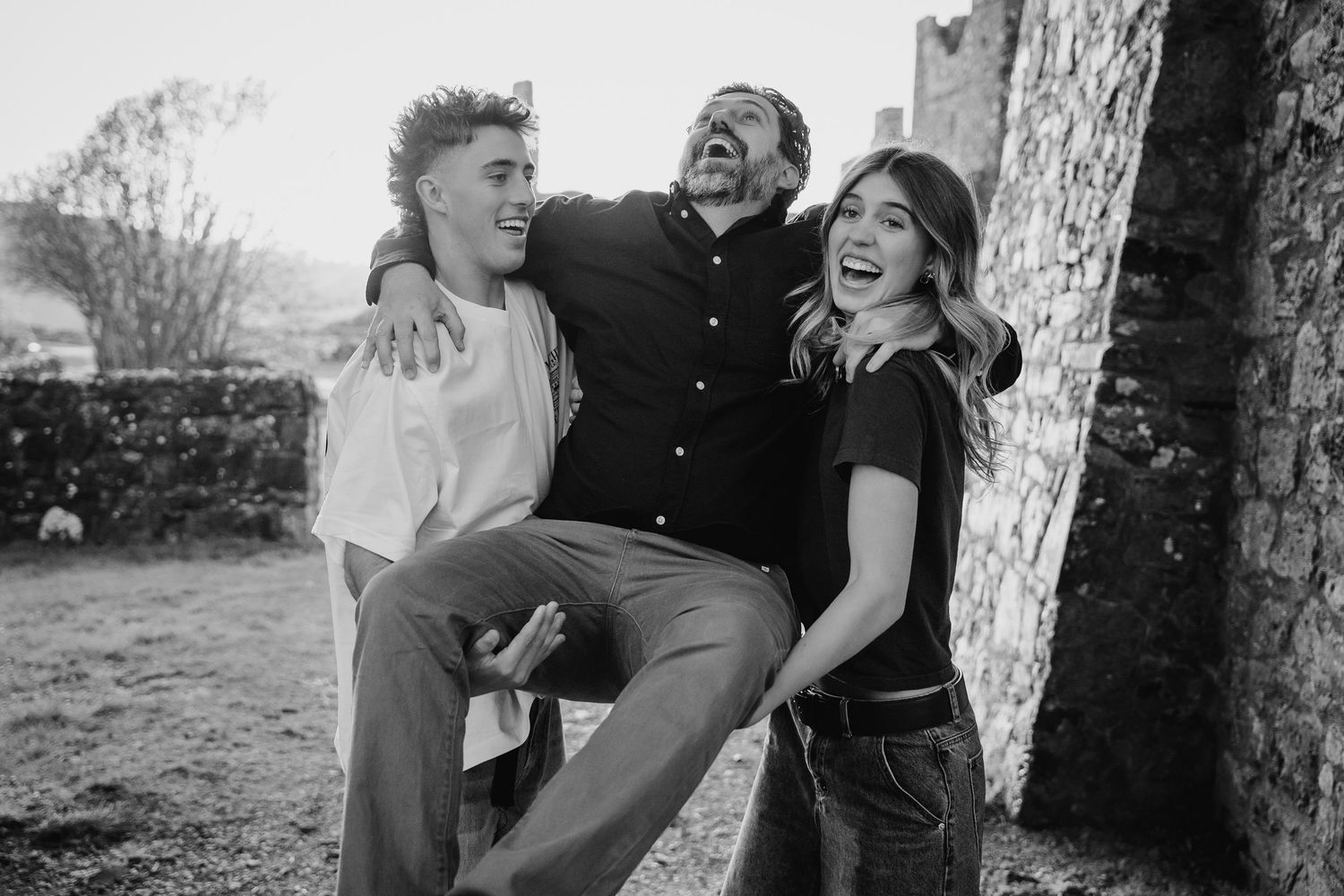 Black and white photo of couple sharing joyful moments against stone castle wall backdrop. Photographer Ireland dublin