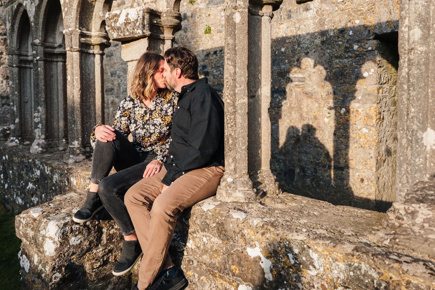 A couple sits together in a romantic moment among ancient stone arches and columns at sunset. Photographer Ireland dublin