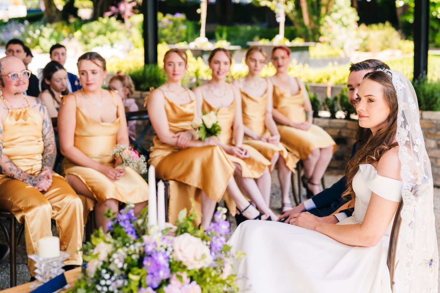 Poulaphouca Wedding photographer wicklow  Wedding party seated outdoors with purple floral arrangements and garden scenery.